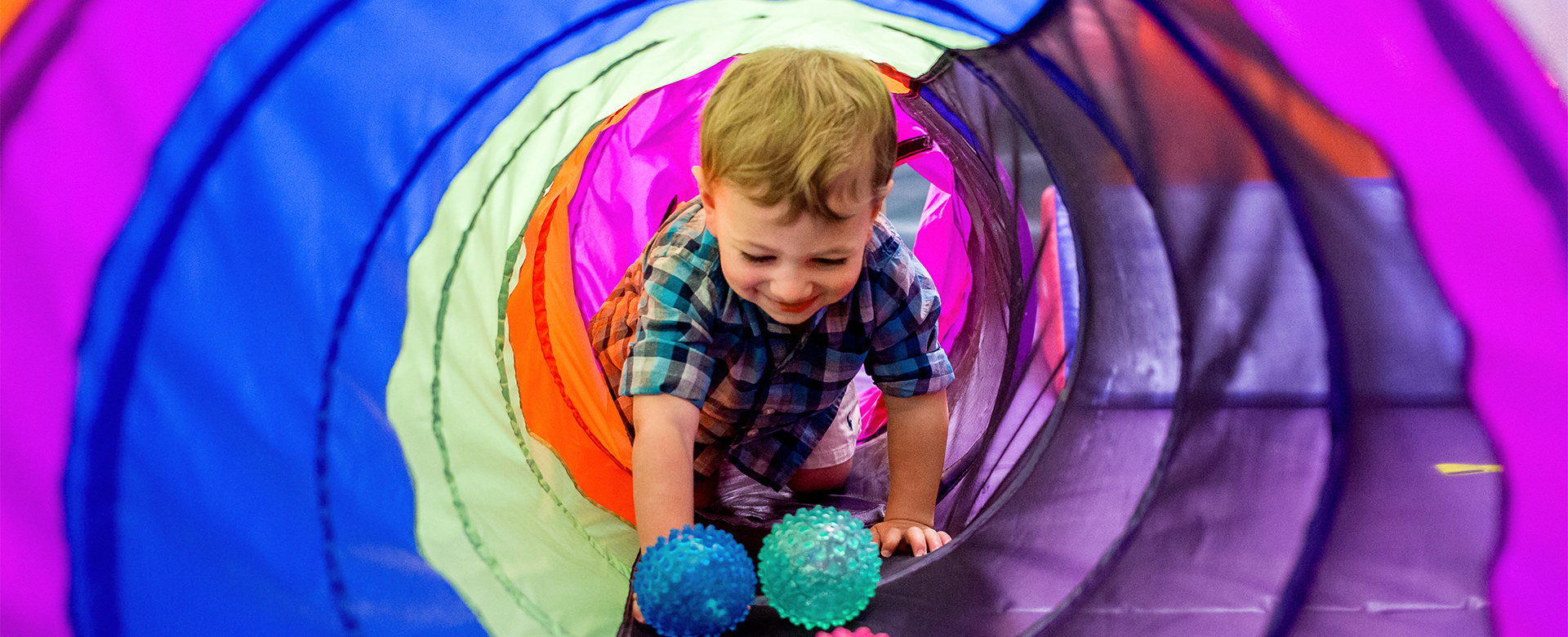 child crawling through colorful tunnel full width