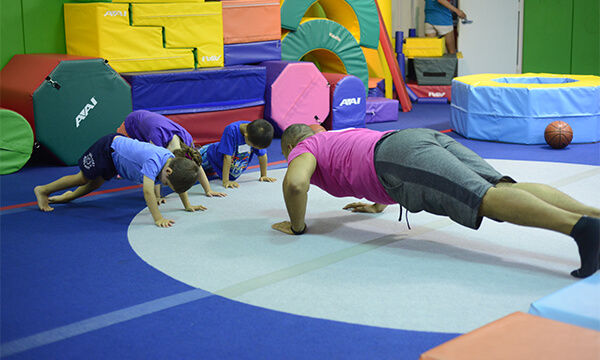 Toddlers copying a coach's push-up pose on the mat during a Kidville gym class