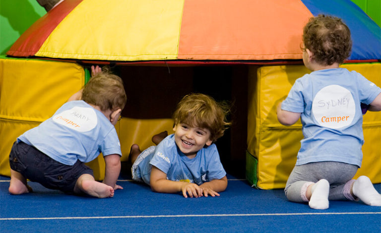 Three toddlers crawling through a soft play tunnel in the Kidville gym