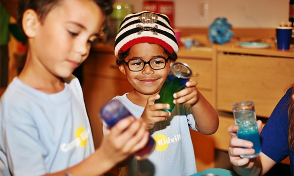 Children holding up colorful discovery tubes during a science exploration at Kidville Upper West Side