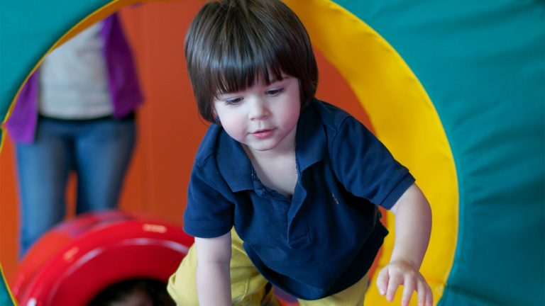 Toddler crawling through a colorful soft tunnel in the Kidville gym