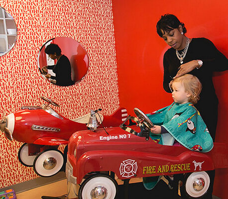Toddler in a fire truck chair getting a haircut from a Kidville stylist