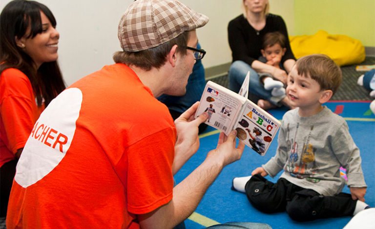 Kidville teacher reading a picture book to a young boy during story time in the classroom