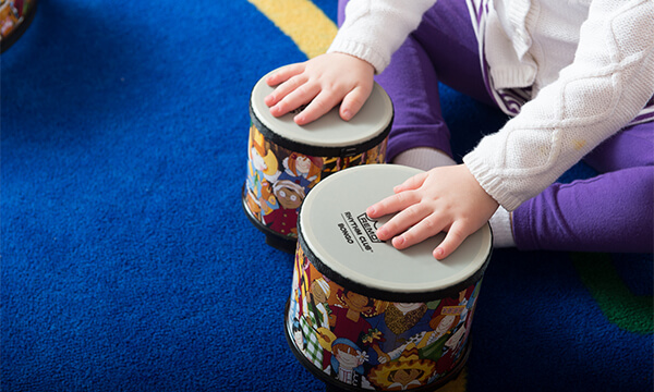 Close-up of a toddler's hands tapping a colorful drum in a Kidville music class