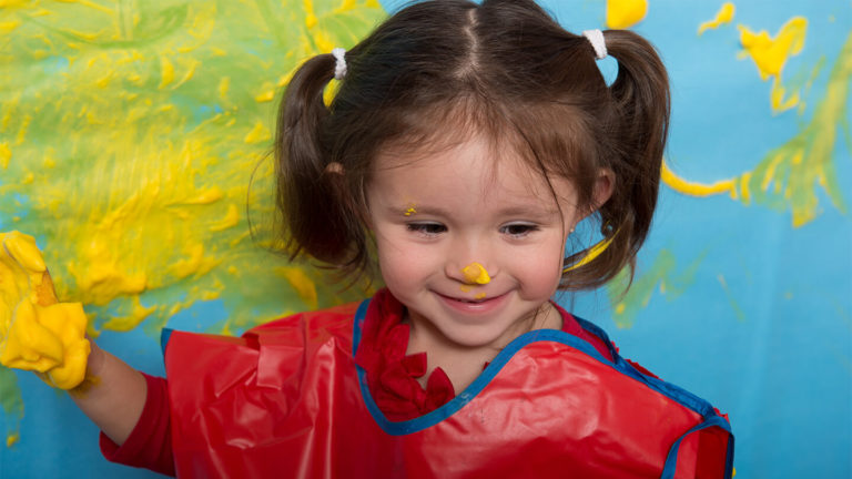 Toddler girl covered in paint and smiling during My Big Messy Art Class at Kidville Upper West Side