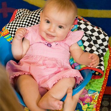 Smiling baby sitting in a blue scoop seat on a colorful play mat