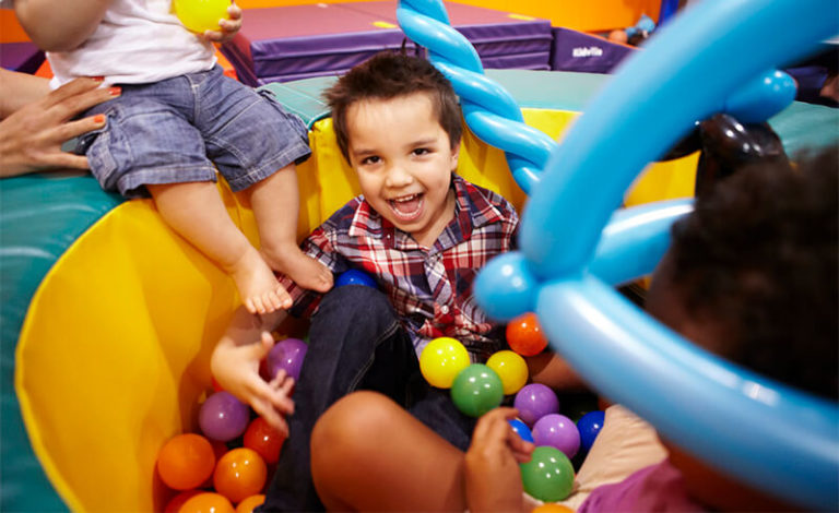 Young boy laughing in a ball pit at the Kidville Upper West Side gym with another child beside him