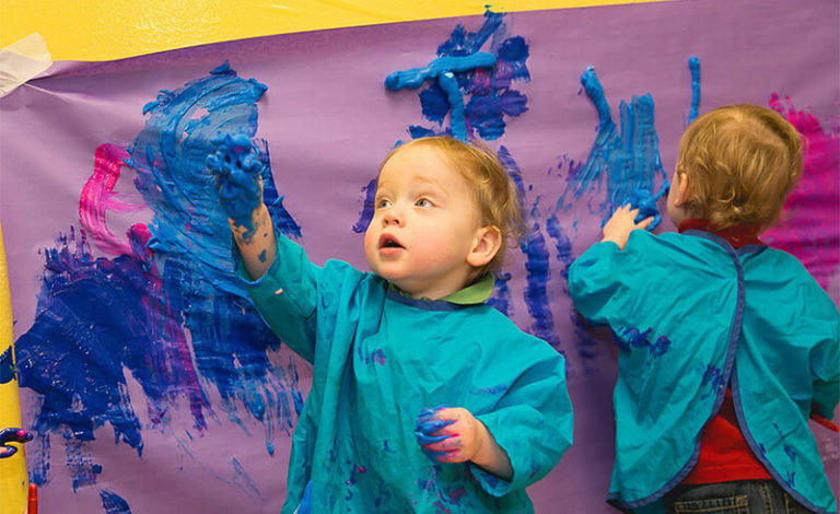Toddlers painting with blue paint on the painting wall in the Kidville art studio