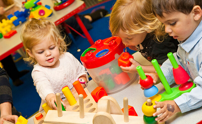Two toddlers playing with colorful stacking toys at a table in the Kidville playspace