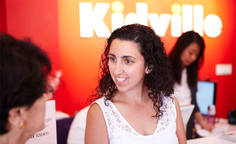 Two parents talking at the Kidville Upper West Side front desk under the orange Kidville sign