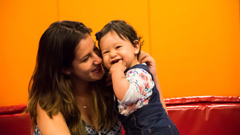 Smiling mom holding her laughing baby against an orange wall