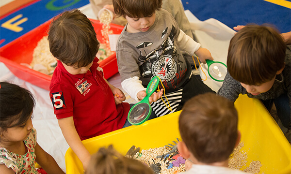 Children squeezing and stretching slime with their hands around a green table at Kidville Upper West Side