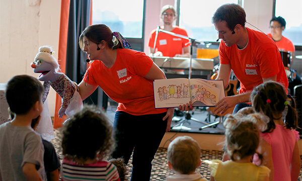 Kidville teachers holding a puppet and a picture book during musical story time with toddlers