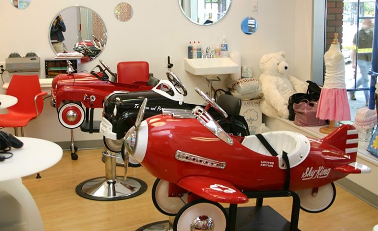 Kids salon chairs shaped like a red airplane and a race car at the Kidville Upper West Side salon