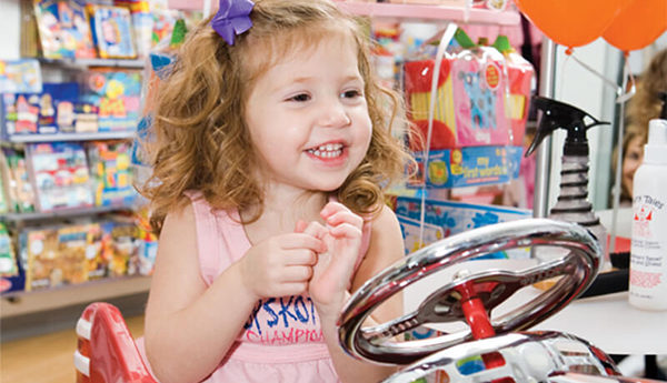 Smiling girl sitting in a toy car chair at the Kidville Upper West Side salon