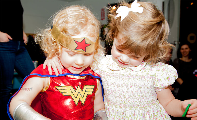 Little girl in a superhero costume hugging a friend at a Kidville birthday party