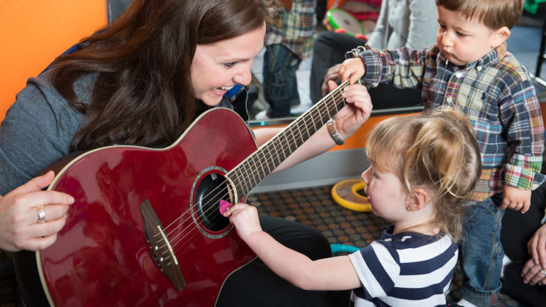 Kidville teacher playing guitar with young children during a music class at Kidville Upper West Side