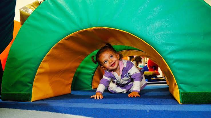 Toddler crawling through a tunnel during a gym class at Kidville Upper West Side